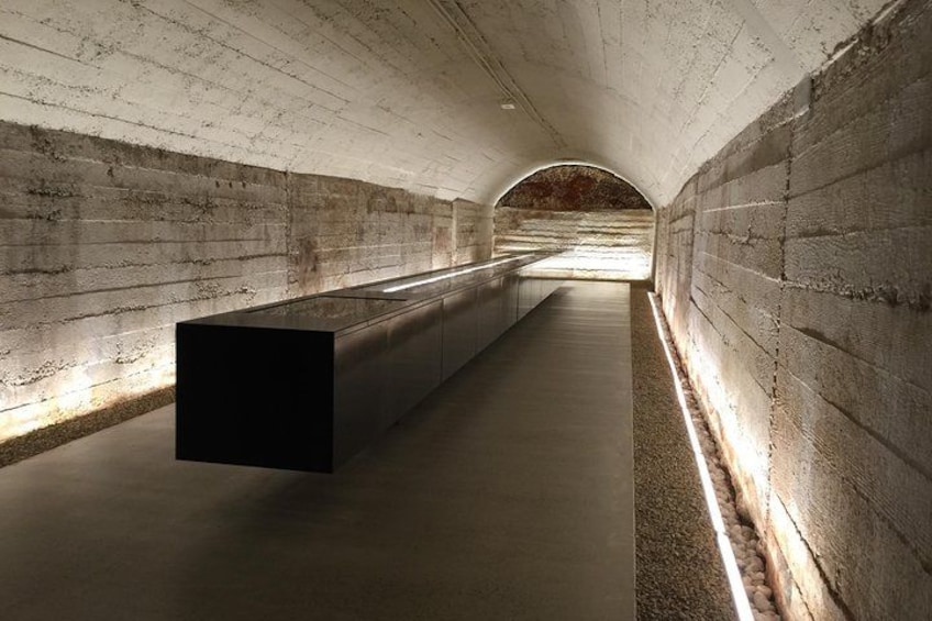 A tunnel with concrete walls, a suspended black cube, and a light source on the right. 1