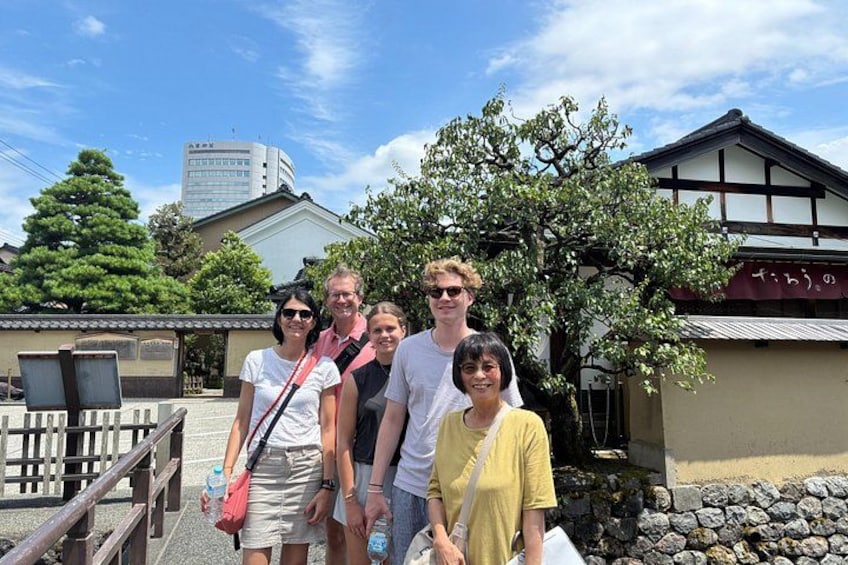 En gruppe mennesker står foran en traditionel japansk bygning med trækonstruktion og stenvæg. 4