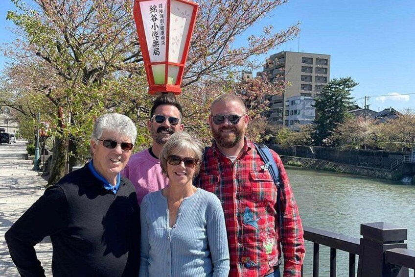 A group of people standing by a river with cherry blossoms and a traditional Japanese lantern in the background. 3