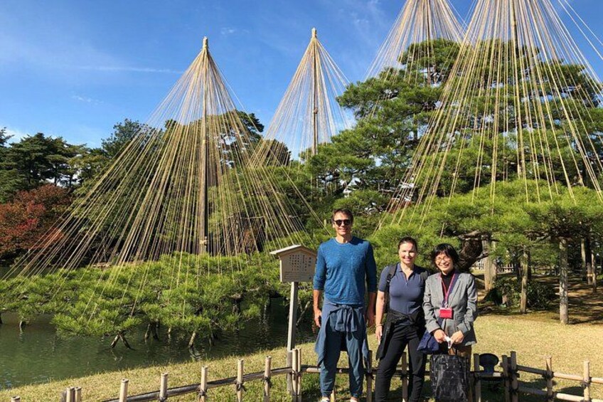 En grupp människor som står framför traditionella japanska byggnader, med en damm och träd i bakgrunden. 5