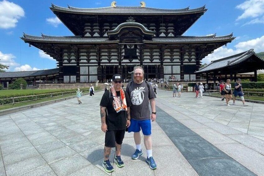 Two people standing in front of a traditional Japanese building with a large, ornate roof. 1