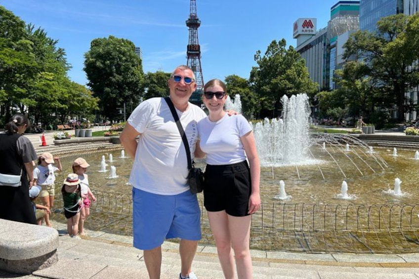 A fountain, a person, and a building with a sign in a park. 1