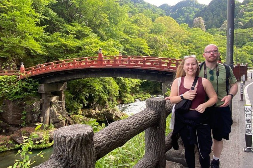 Eine rote Brücke über einem Fluss, umgeben von üppigem Grün und einem Steinpfosten. 2