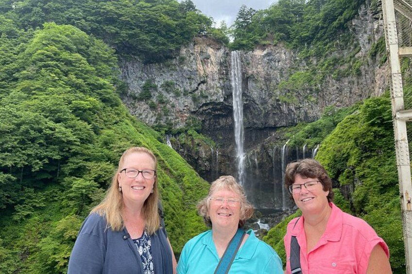 Three people standing in front of a waterfall with lush greenery and rocky cliffs. 2