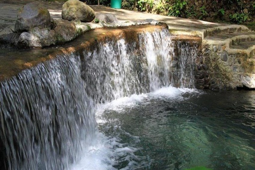 A waterfall cascading over a stone ledge into a pool, surrounded by rocks and greenery. 2