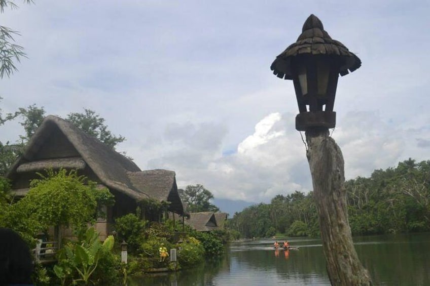 A thatched-roof house, a lamp post, and a calm river with a boat. 2