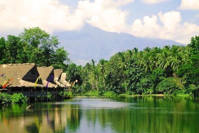 A river with thatched-roof huts and dense greenery. 1