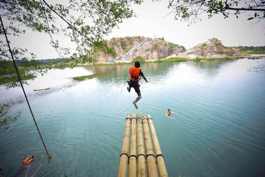 A person jumping from a bamboo raft into a calm river surrounded by rocky cliffs. 1