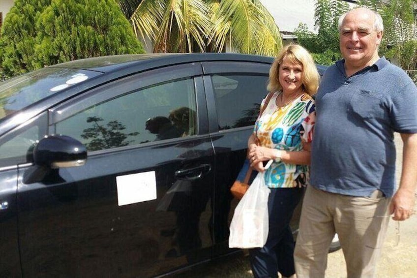 A black car, a person in a blue shirt, and another in a colorful top. 2