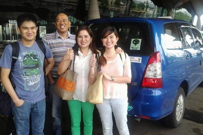 A group of people standing in front of a blue car with a license plate. 1