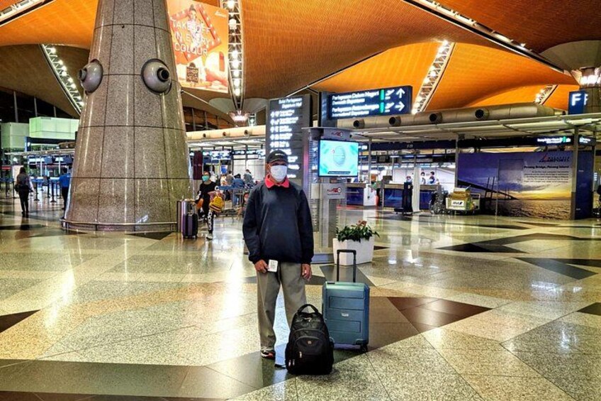 A man standing in a modern airport terminal with a suitcase and a backpack. 2