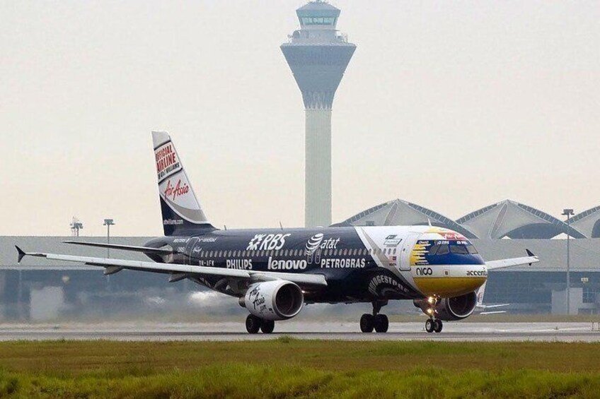 An airplane with multiple logos on its body, including Petrobras and Lenovo, taxiing on a runway with a control tower in the background. 1