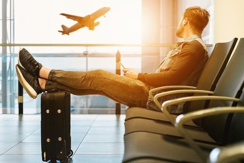 A person sitting on a bench in an airport, leaning back with a suitcase beside them. 2