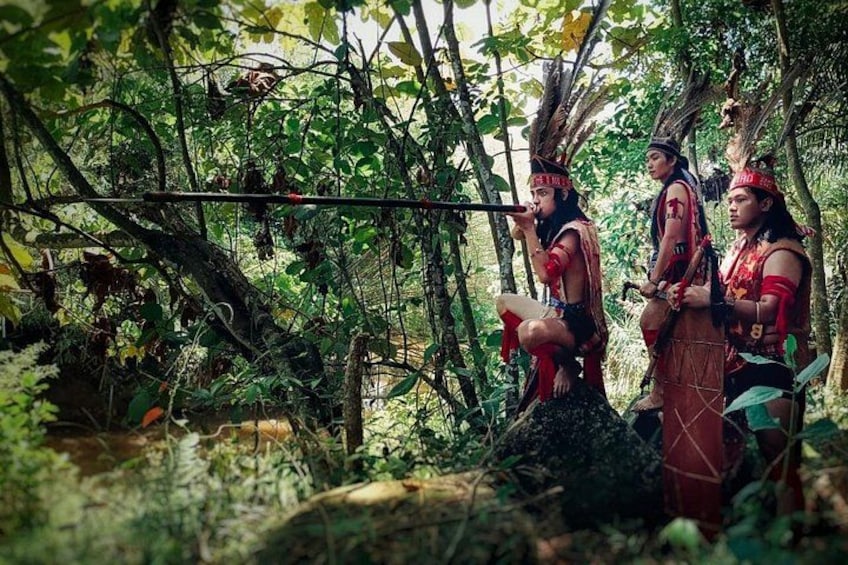 Tre persone in abiti tradizionali in una zona boschiva con fitta vegetazione e un albero caduto. 2