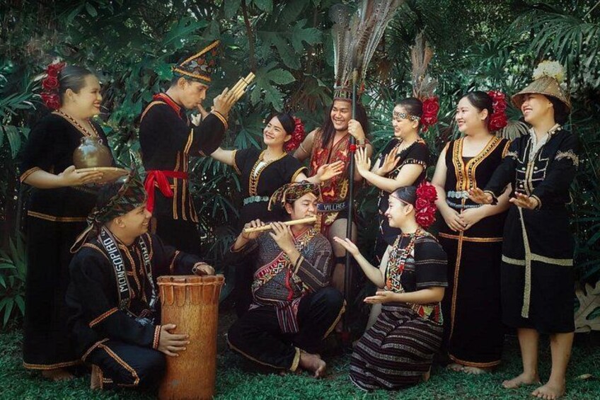 Un gruppo di persone in abiti tradizionali, alcune che suonano strumenti musicali, in un ambiente naturale verdeggiante. 4