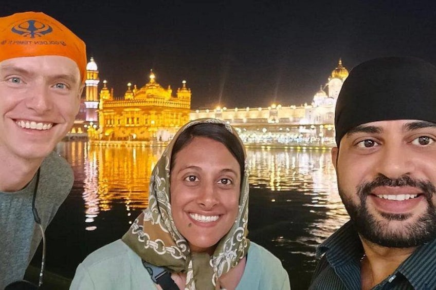 Three people in front of the Golden Temple at night. 1