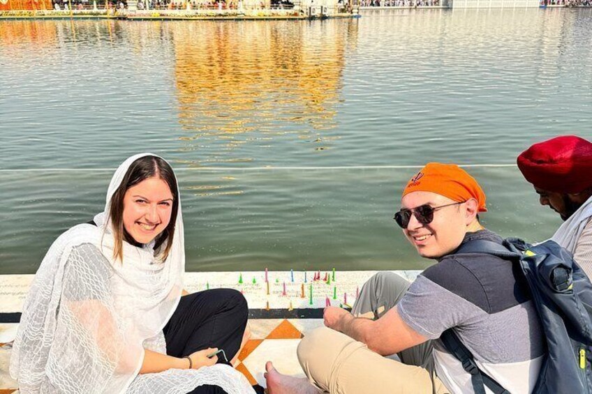 Three people sitting by a calm body of water, with a reflection of a building in the background. 4