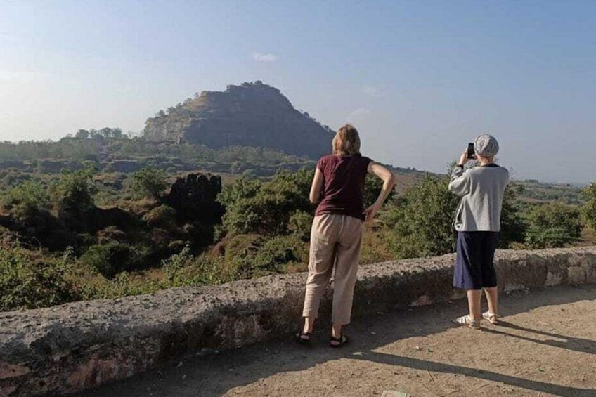 Two people standing on a dirt path, overlooking a rocky hill with sparse vegetation. 2
