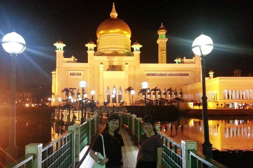 A mosque with a golden dome and minarets, illuminated by street lamps, with a reflection in the water. 2