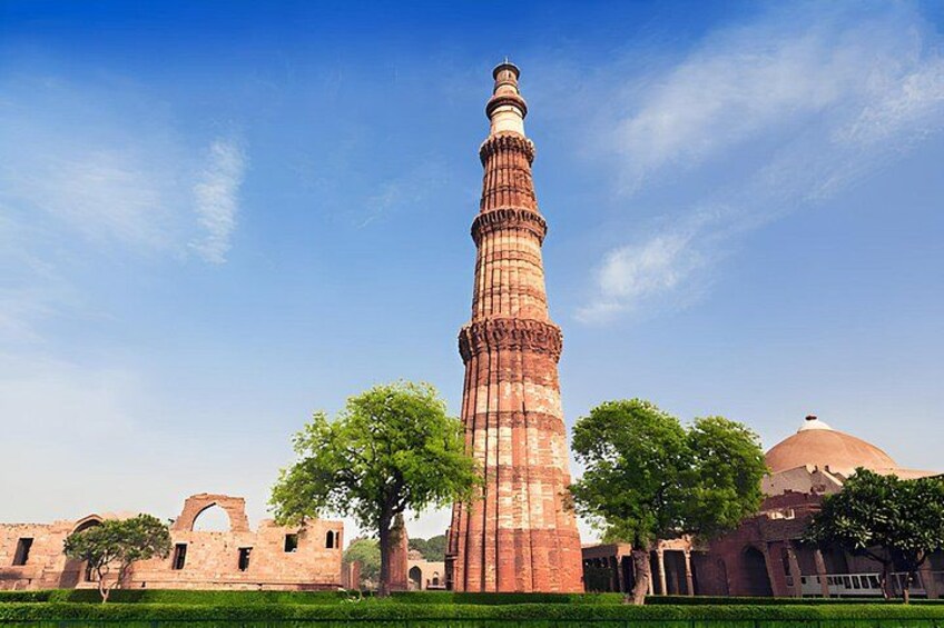 Een hoge minaret met een koepel, omgeven door bomen en historische gebouwen. 1