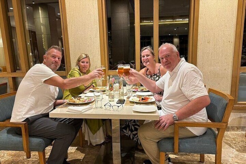 Cuatro personas sentadas en una mesa con comida y bebidas, brindando con copas. 5