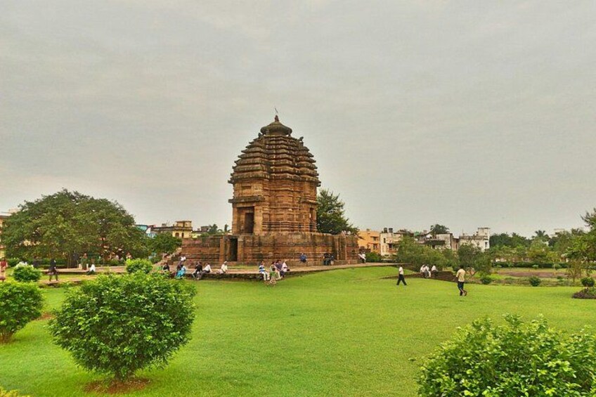 A historic temple with a tiered tower, surrounded by a grassy area with scattered trees and people. 4