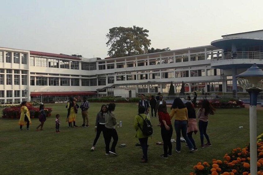 A group of people in a grassy area in front of a modern building with multiple windows and a dome structure. 5