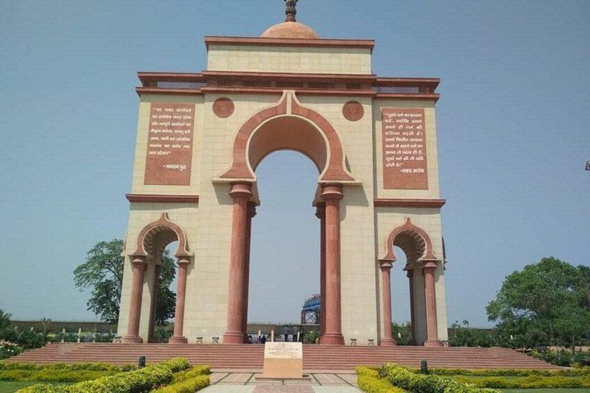 A large arch monument with inscriptions, surrounded by well-maintained greenery and a clear sky. 1