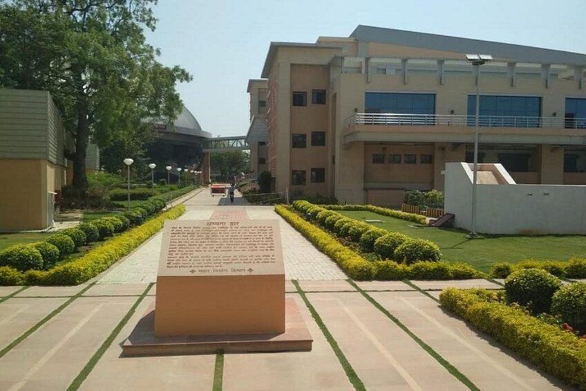 A pathway leading to a building with a plaque, surrounded by neatly trimmed bushes and trees. 3