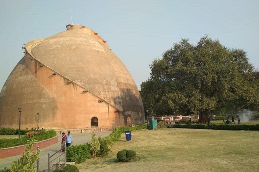 A large, dome-shaped building with a curved roof, surrounded by a grassy area and a large tree. 4