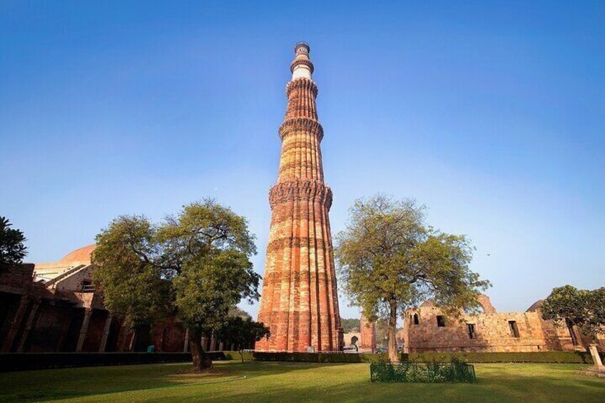 The Qutub Minar, a tall, slender tower with intricate carvings, surrounded by trees and ancient buildings. 5