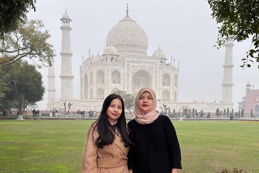Two people standing in front of the Taj Mahal with its domes and minarets visible. 5