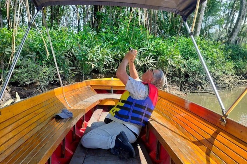 A man in a boat wearing a life jacket, surrounded by dense greenery. 5