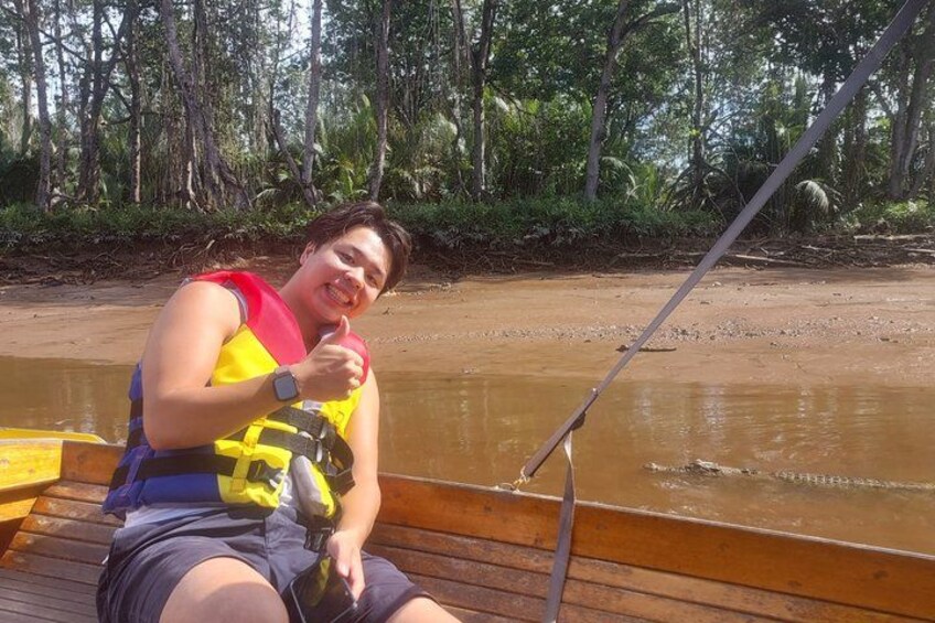 Une personne assise sur une jetée en bois, tenant une canne à pêche, avec une rivière et des arbres en arrière-plan. 5