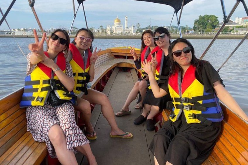 A group of people on a boat with life jackets, a wooden deck, and a cityscape with a prominent building in the background. 2