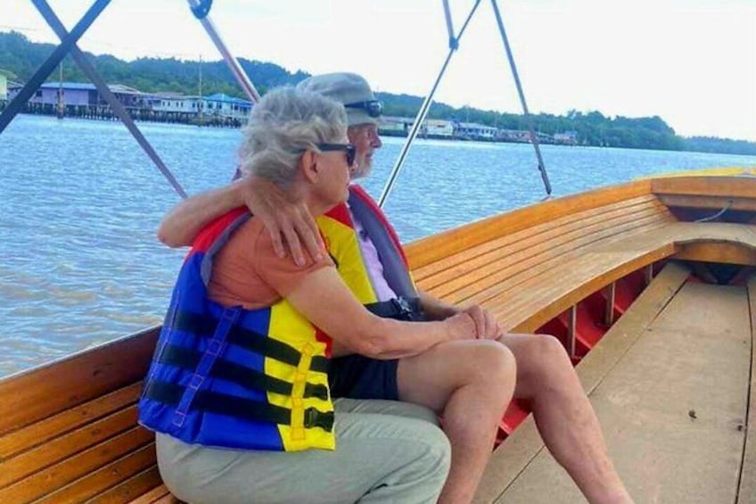 Two people on a wooden boat, wearing life jackets, with water and a dock in the background. 4