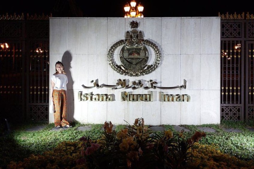 A person standing in front of a sign with Arabic text and a coat of arms. 1