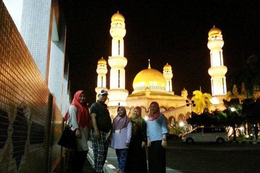 A group of people standing in front of a mosque with illuminated minarets and a dome at night. 2