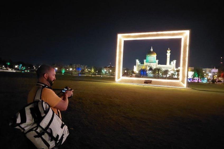A person taking a photo of a building framed by a lighted rectangle at night. 5