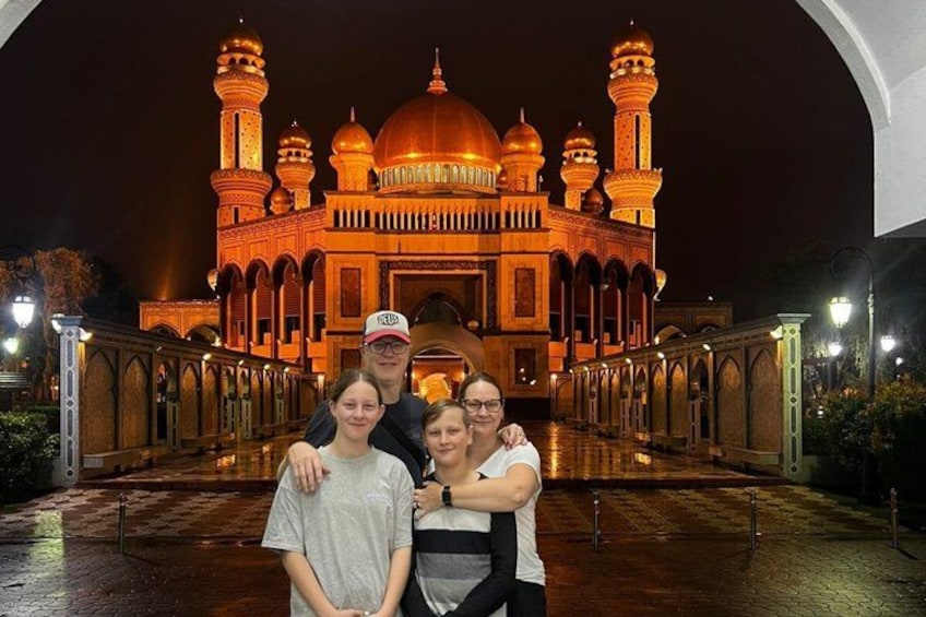 A group of people in front of a mosque with illuminated domes and minarets at night. 4