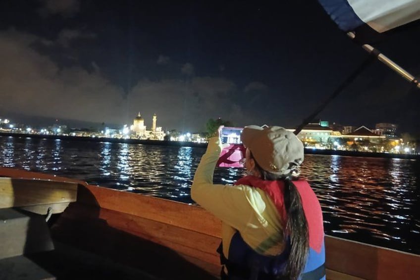 A person on a boat, facing a cityscape with illuminated buildings and a prominent tower. 2