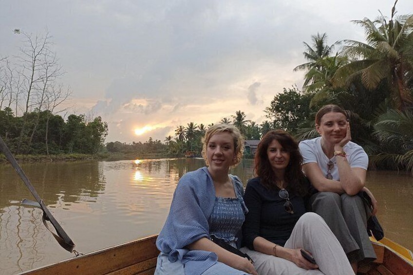 Trois personnes dans un bateau sur une rivière paisible, avec des palmiers et un coucher de soleil en arrière-plan. 5