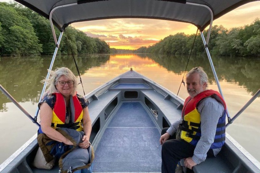 Two people on a boat with life jackets, a calm river, and trees along the banks. 1