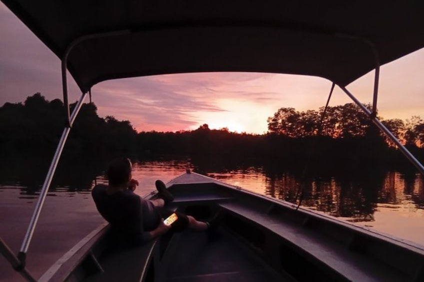 A person sitting on a boat at sunset, holding a device. 3
