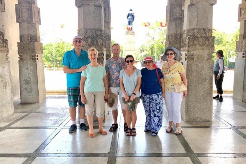 A group of people standing under a covered area with stone columns and a statue in the background. 3