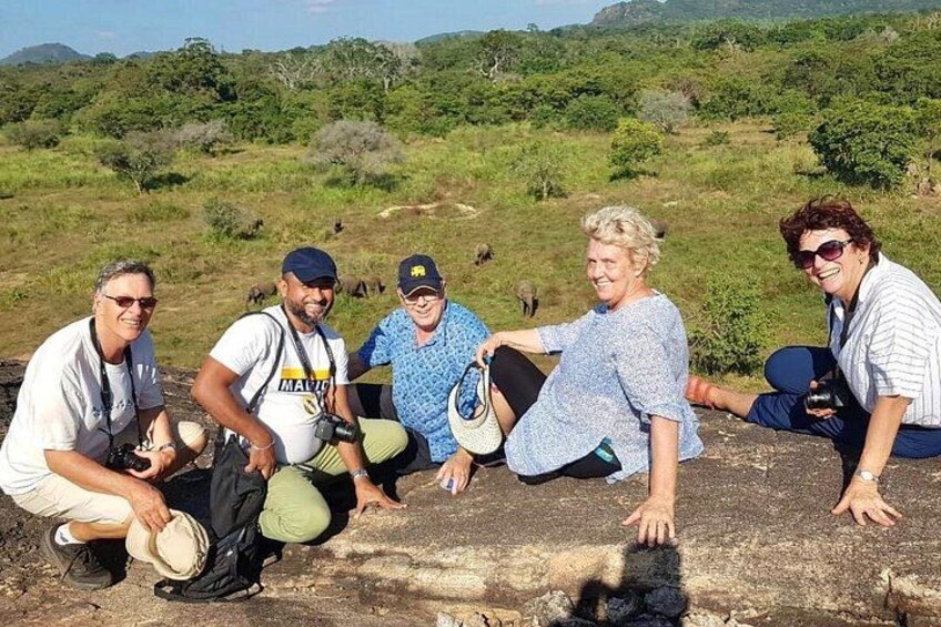 Un grupo de personas sentadas sobre una roca, con un paisaje cubierto de hierba y árboles al fondo. 2