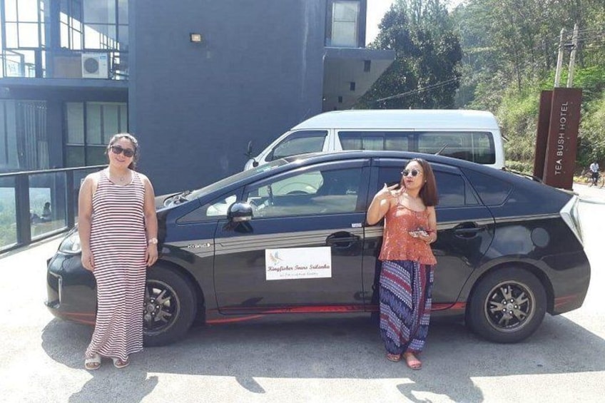 Dos mujeres de pie junto a un coche negro con un letrero que dice 'Teabush Hotel'. 4
