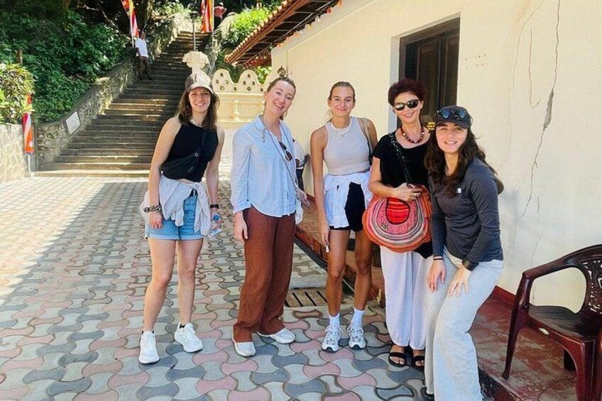 A group of people standing on a patterned pavement, a staircase, and a building with a white wall and a door. 4