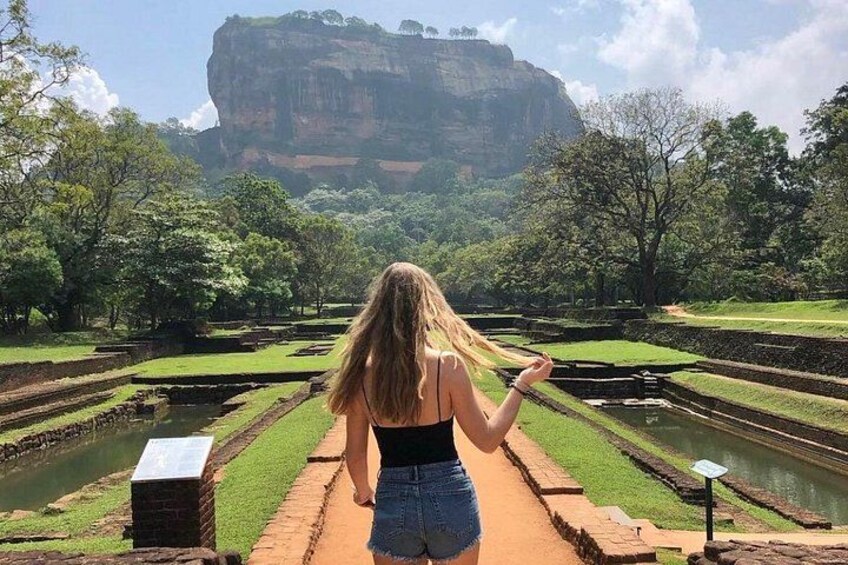 A person walking on a pathway with terraced fields and a large rock formation in the background. 1