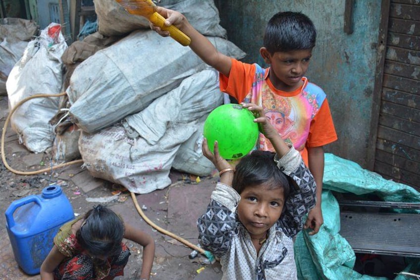 Children playing with a green ball in an outdoor setting with sacks and a blue container in the background. 4